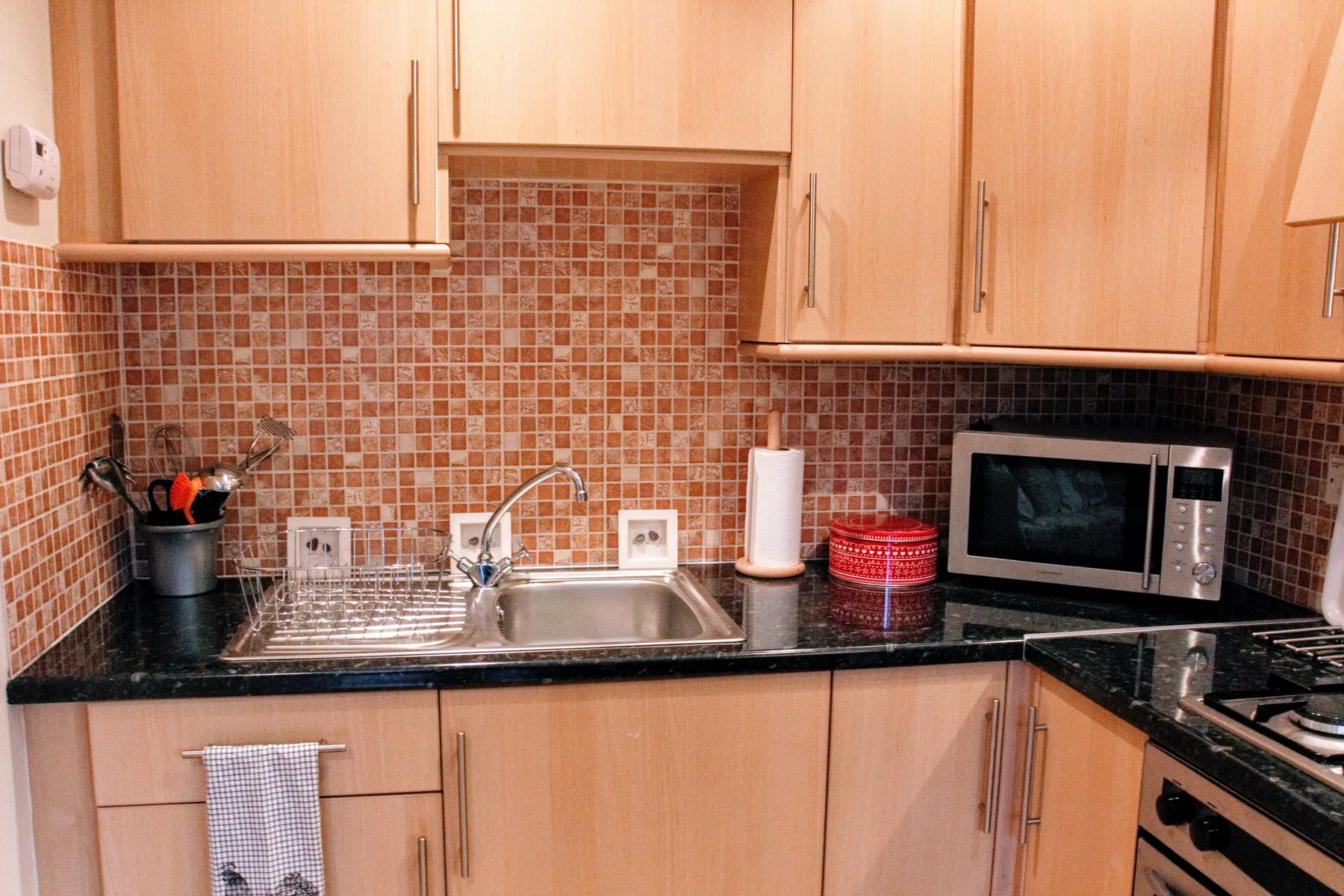 A kitchen counter with a sink, microwave, and tiled backsplash.