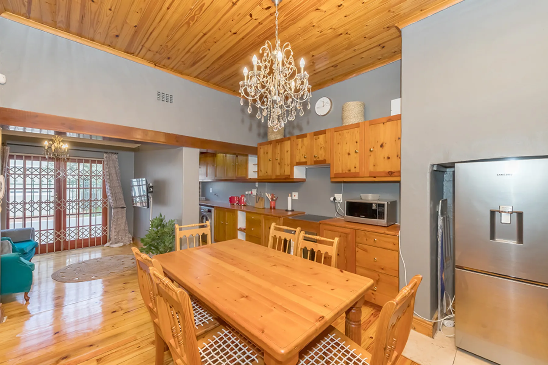 A wood dining table sits beside an open kitchen with wooden cabinets.