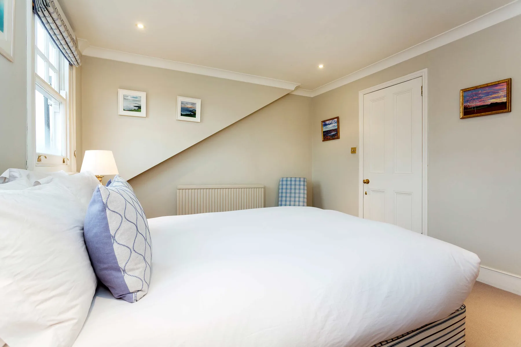A bright bedroom with a neatly made bed beneath a sloped ceiling.