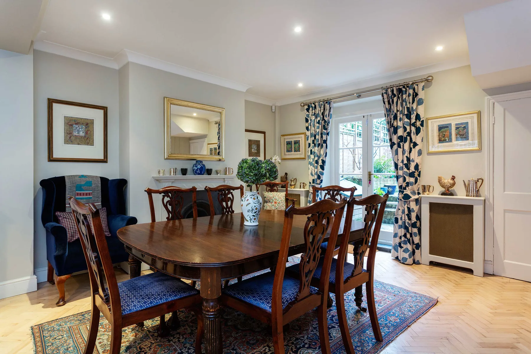 A dining room with a wooden table and chairs beside bright windows.
