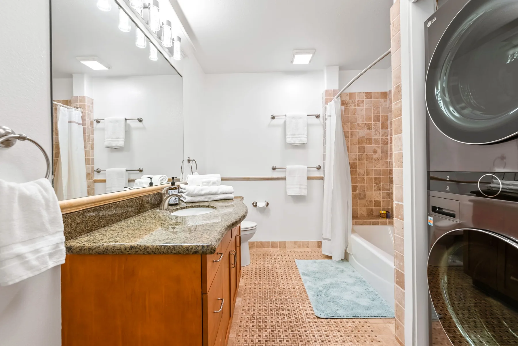Un baño luminoso con lavabo, bañera y lavadora y secadora apiladas.