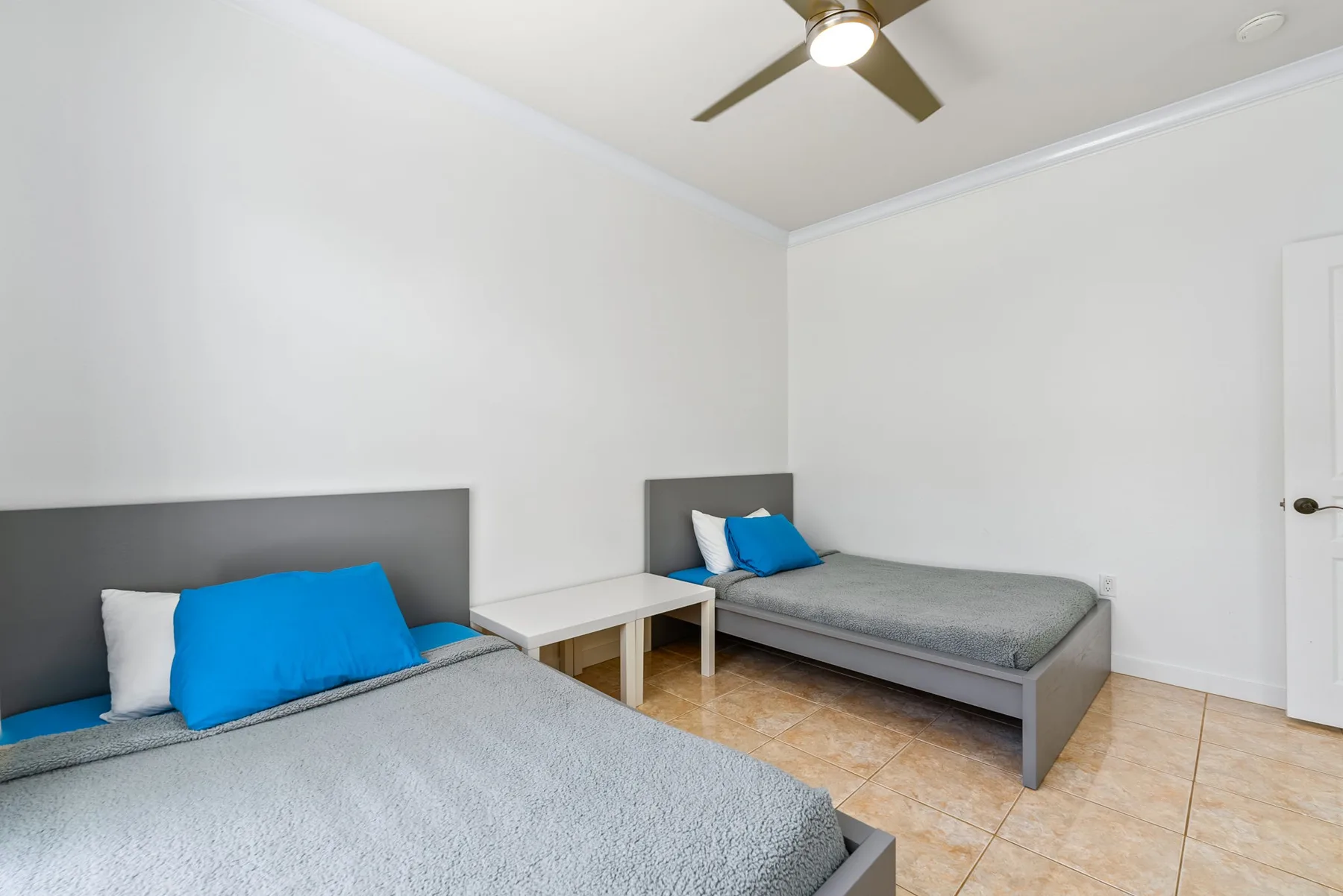 Un dormitorio con dos camas, ropa de cama gris y una mesita entre ellas.