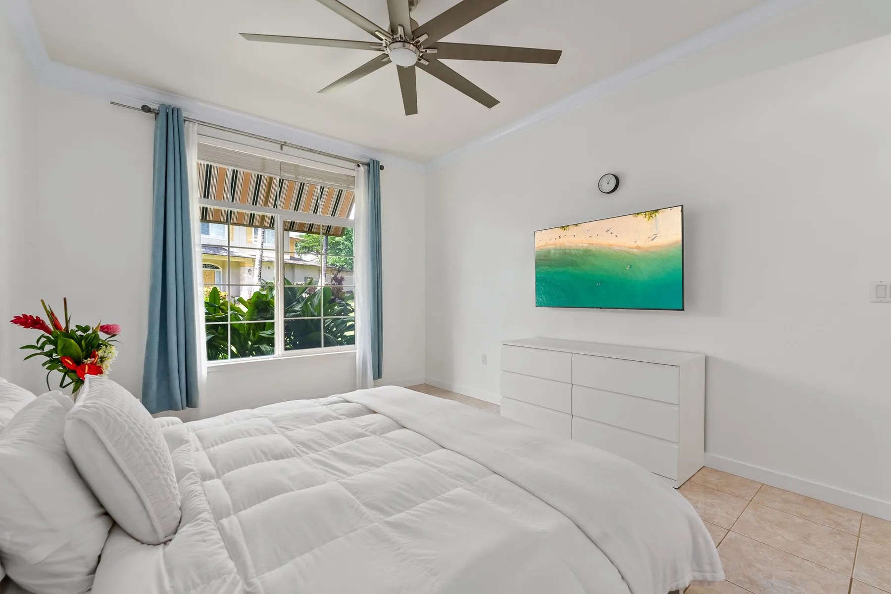 Un dormitorio luminoso con una cama grande, una ventana y un ventilador de techo.