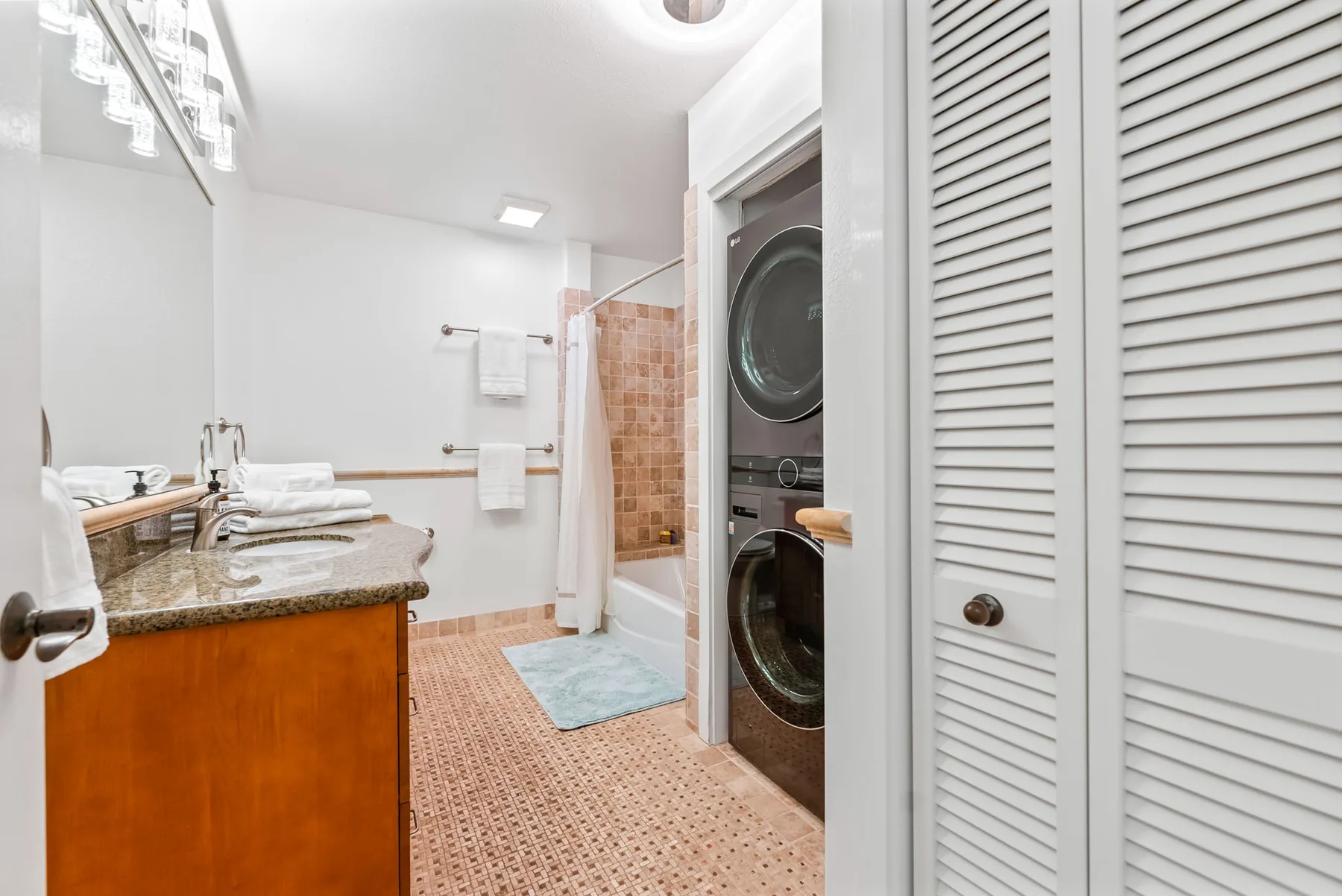 Un baño luminoso con lavabo, bañera y lavadora y secadora apiladas.