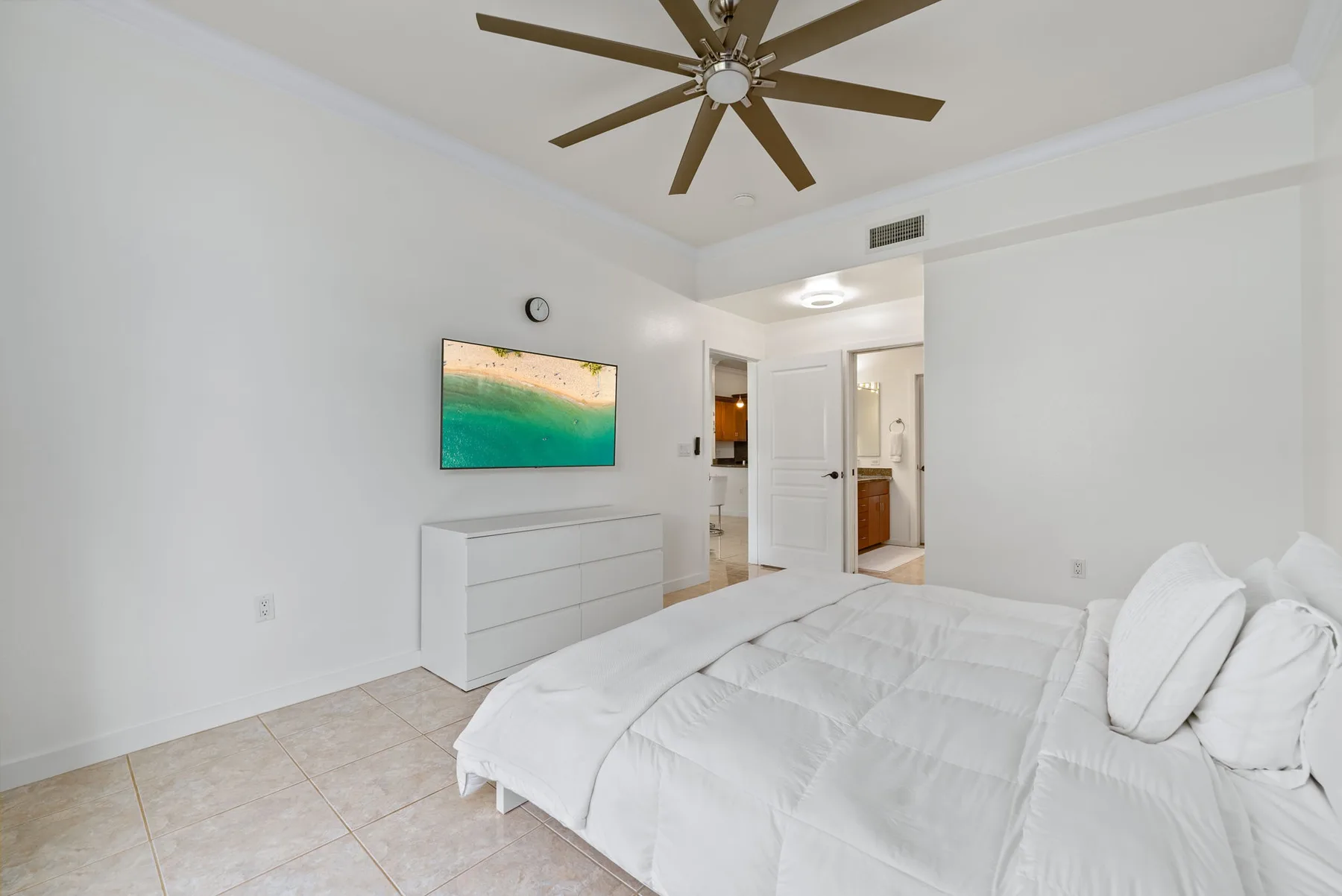 Un dormitorio luminoso con ropa de cama blanca y un televisor en la pared.