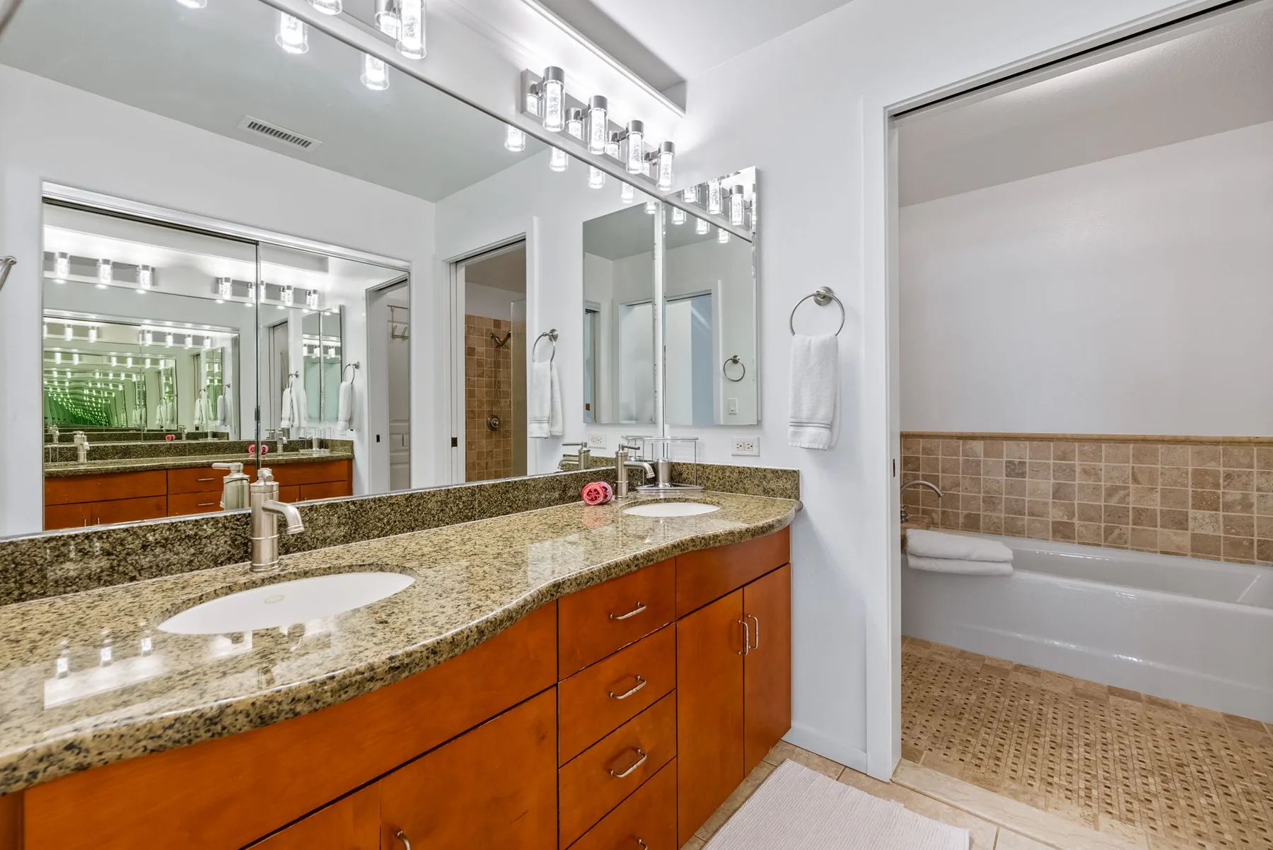 Un baño luminoso con un tocador largo, un espejo amplio y una bañera.