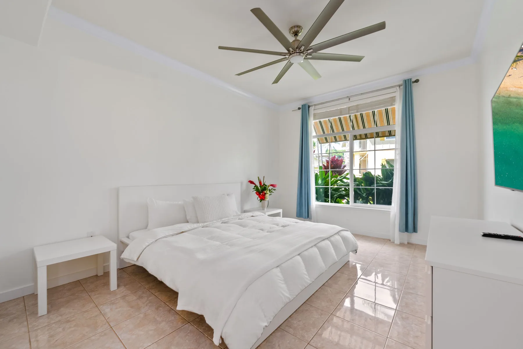 Un dormitorio luminoso con una cama blanca junto a una ventana con cortinas azules.