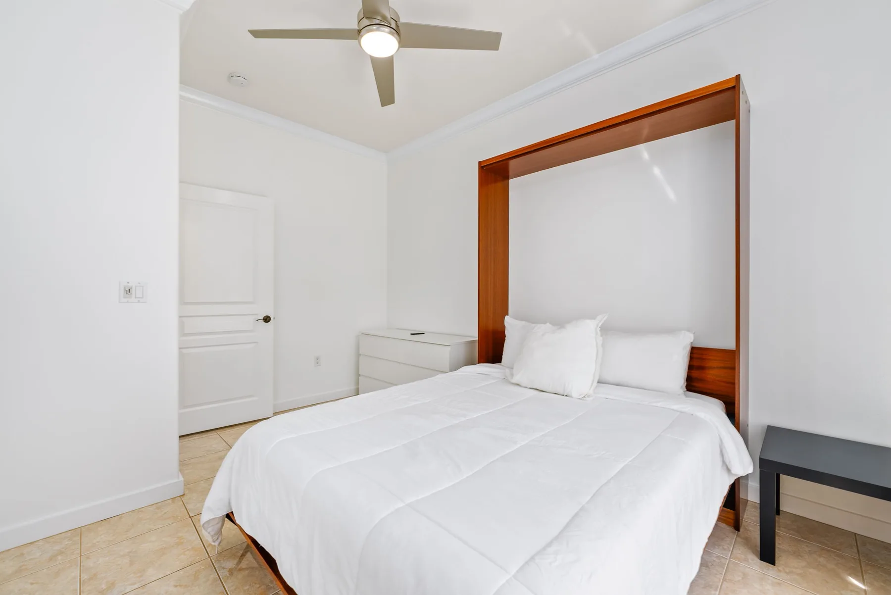 Un dormitorio luminoso con una cama grande, ropa de cama blanca y un ventilador de techo.