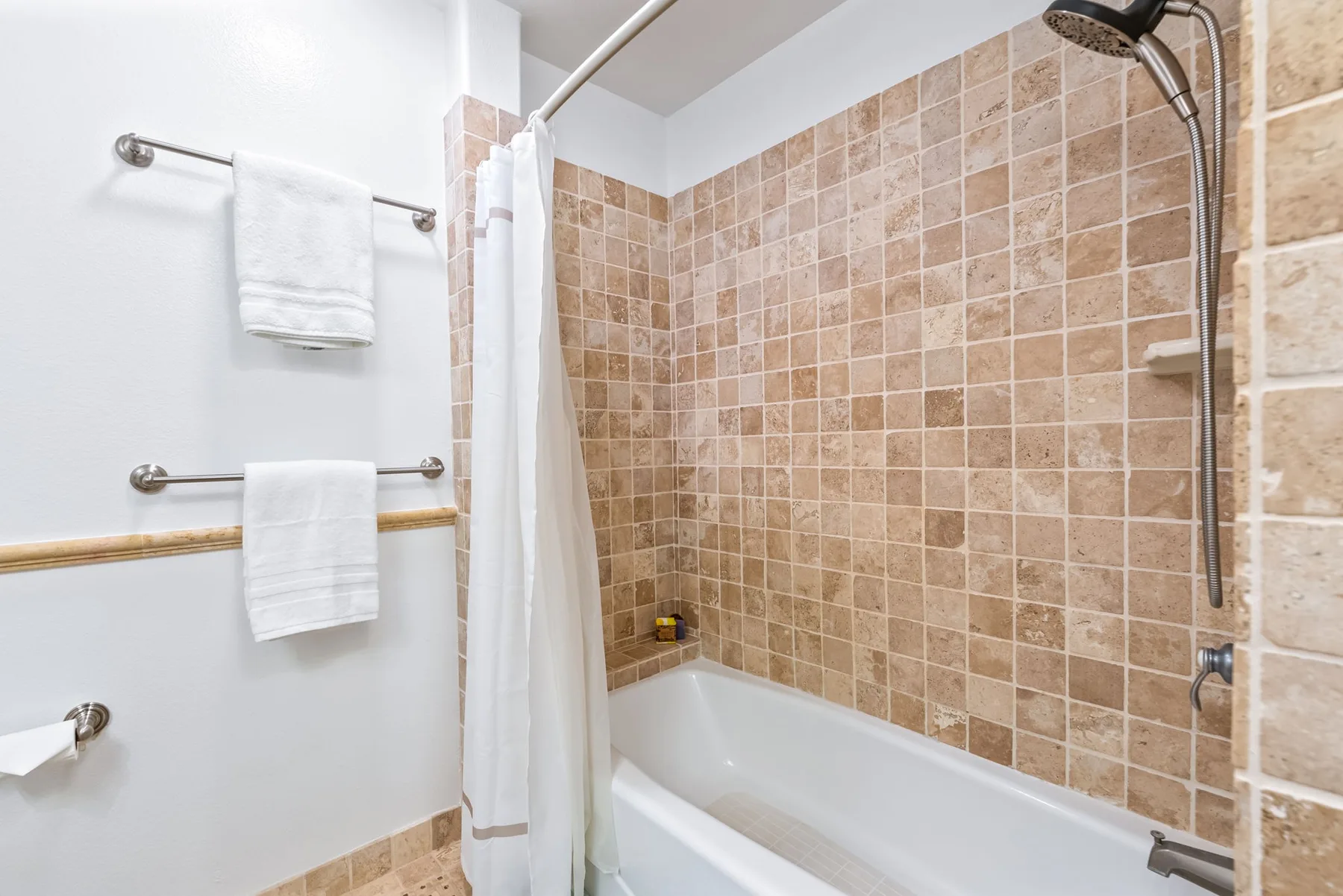 Un baño alicatado con bañera, ducha y cortina blanca.