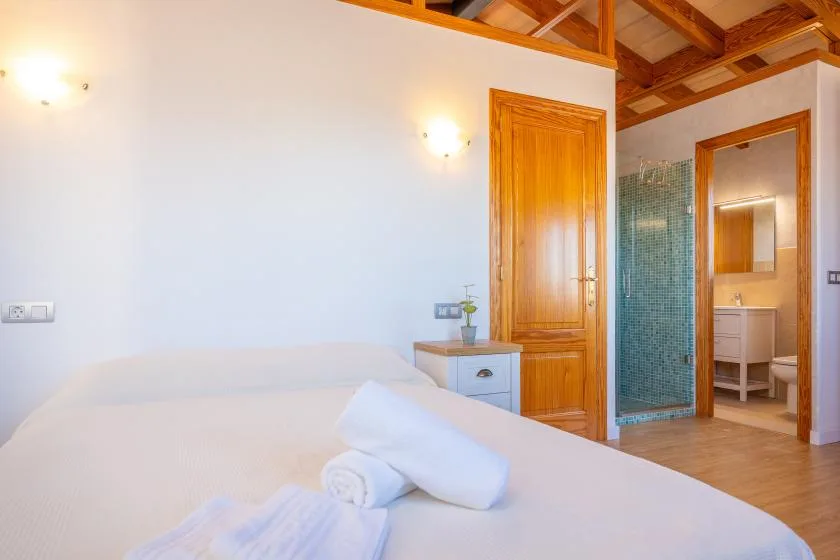 A bedroom with a neatly made bed and wooden ceiling beams.