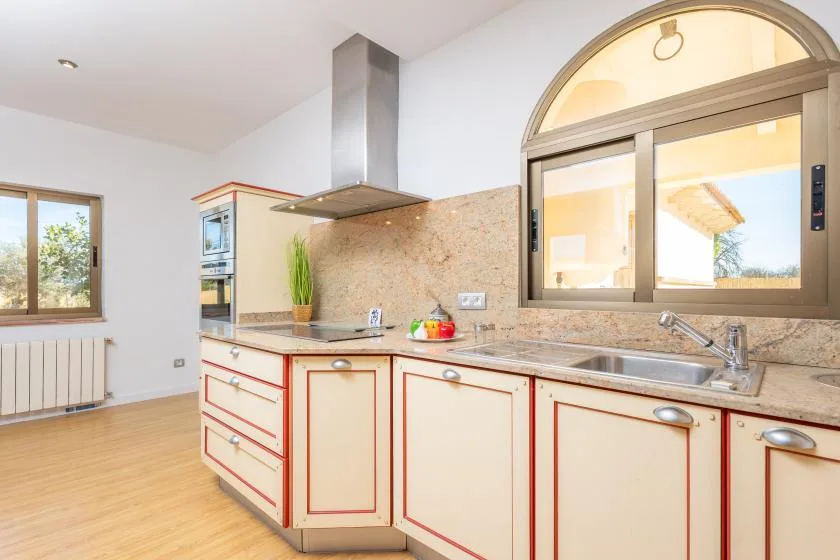 A bright kitchen with pale cabinetry, a countertop, and a sink beneath an arched window.