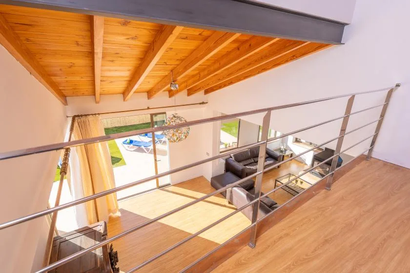 A wooden loft overlooks a bright living area behind a metal railing.