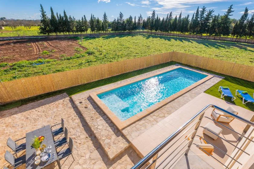 An outdoor swimming pool sits beside a stone-paved patio and green lawn.
