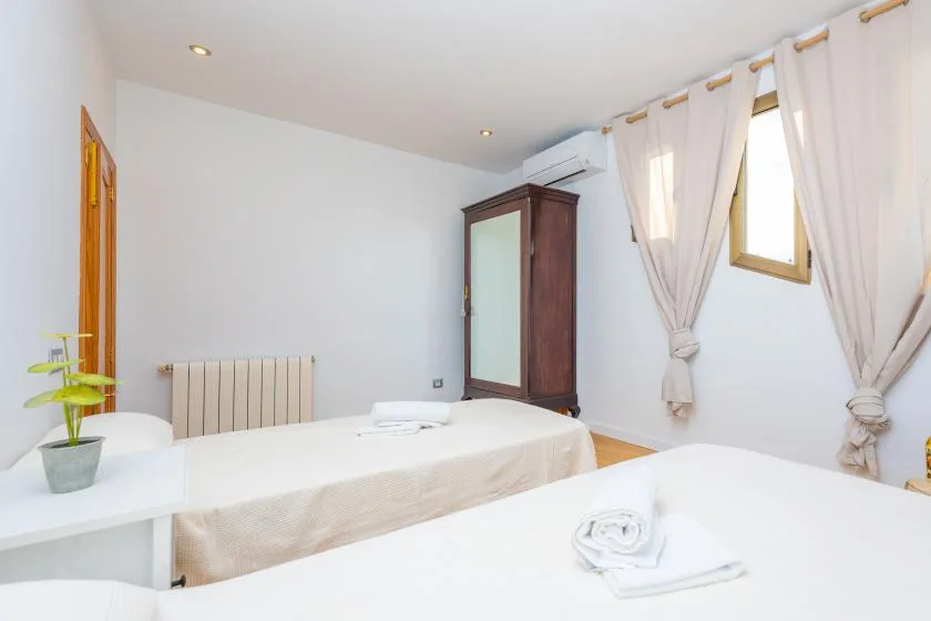 A bright bedroom with two beds and curtains around a window.