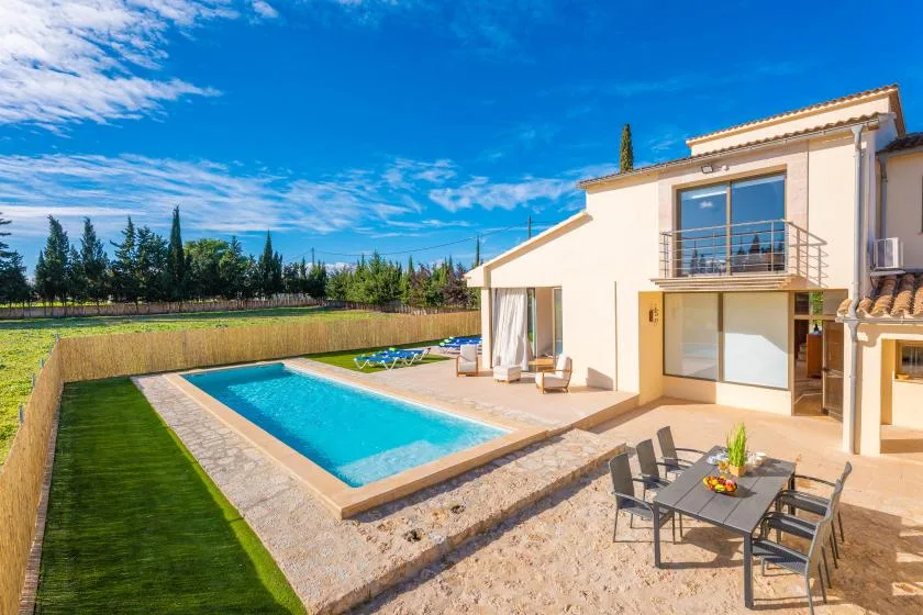 A sunny outdoor pool sits beside a modern house and patio seating.