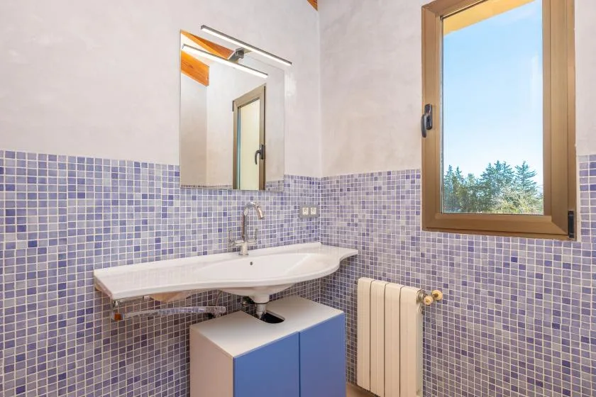 A bathroom vanity with a sink sits beneath a mirror beside a window.