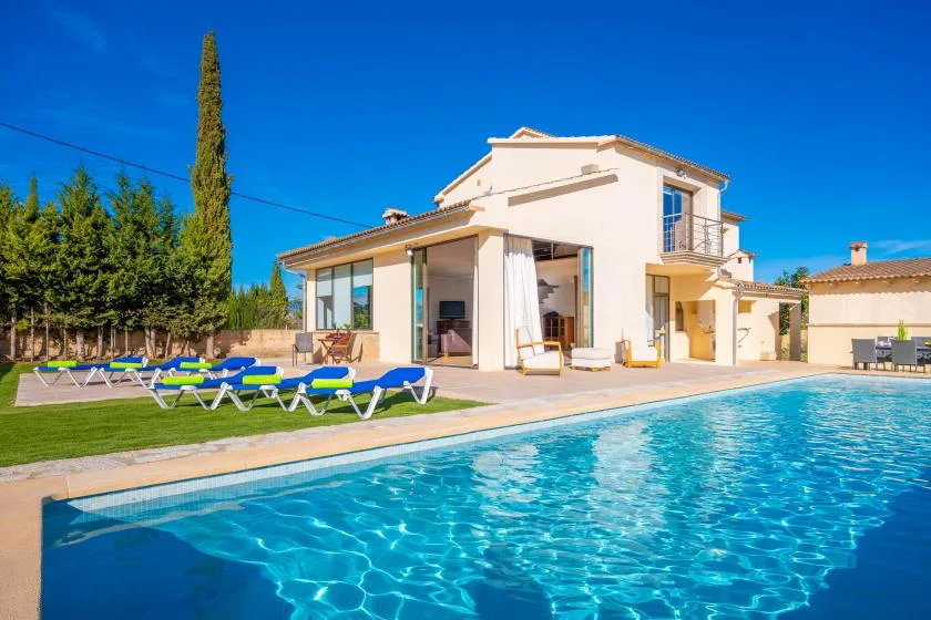 A house beside a swimming pool, with lounge chairs arranged on the lawn.