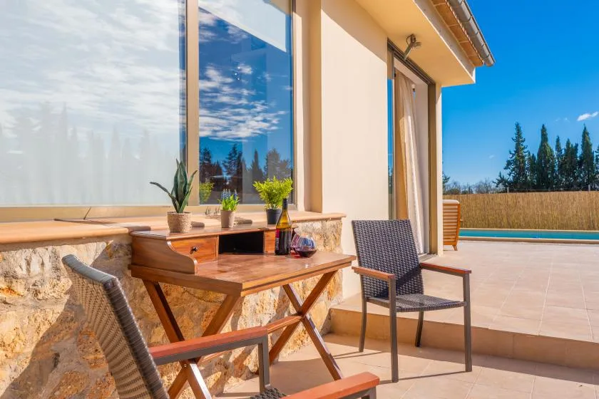 A sunny patio beside large windows, with a wooden table and outdoor seating.