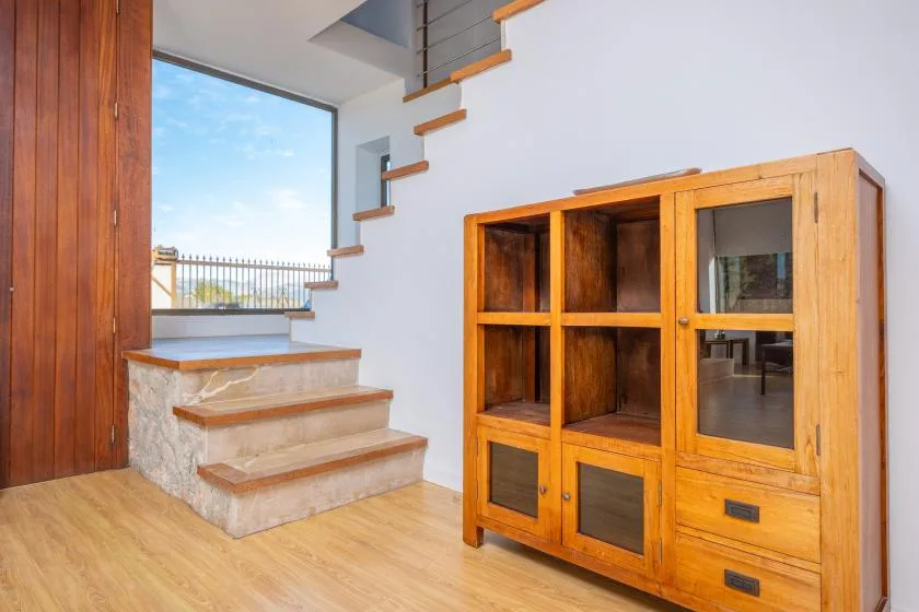 A bright interior with wooden stairs beside a large wooden cabinet.