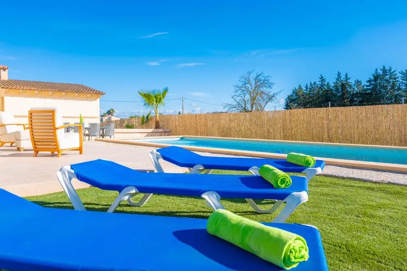 Outdoor poolside lounge area with blue sun loungers and green towels.