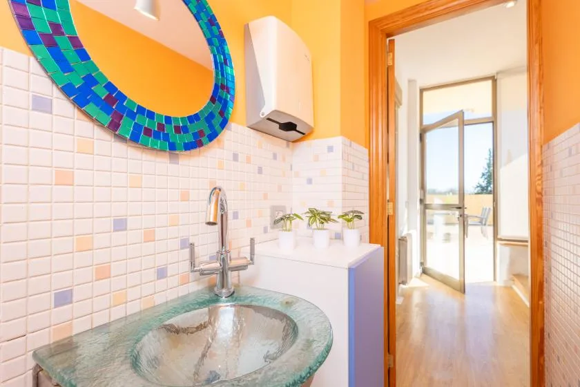 A colorful bathroom sink beneath a mosaic mirror, with an open doorway.