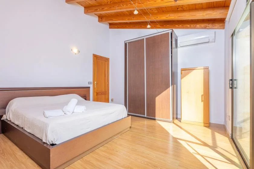 A bedroom with a bed, a wardrobe, and exposed wooden ceiling beams.