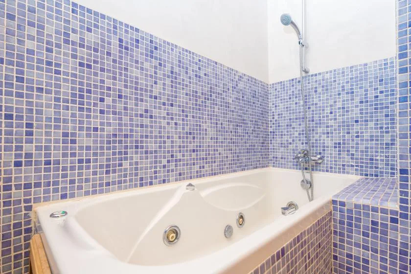 A tiled bathroom with a built-in jetted bathtub and wall-mounted shower.