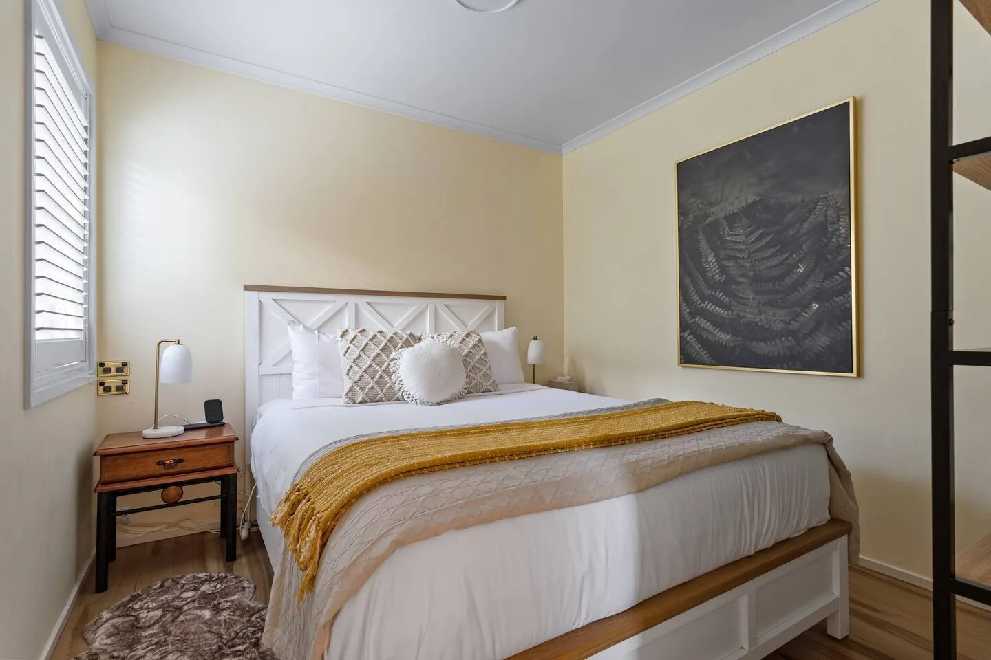 A bedroom with a bed dressed in white bedding and a gold throw.