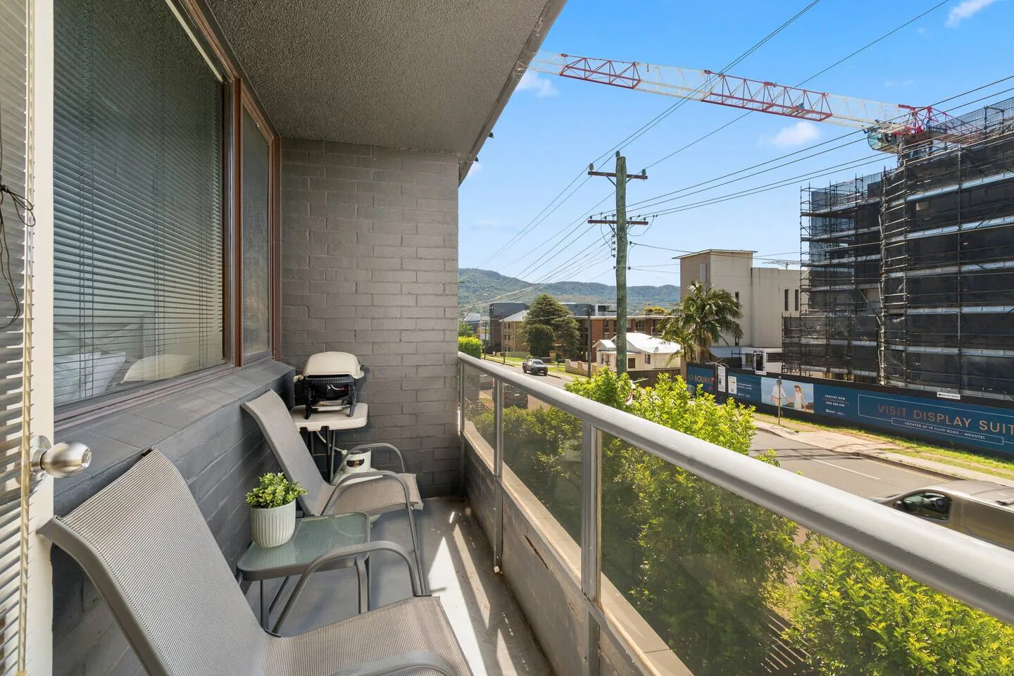 A balcony has outdoor seating and a small potted plant overlooking nearby buildings.