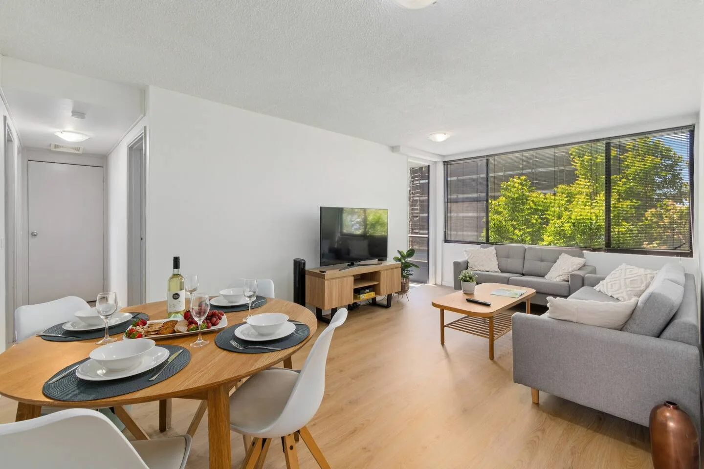 A bright living and dining area with a large window and a television.