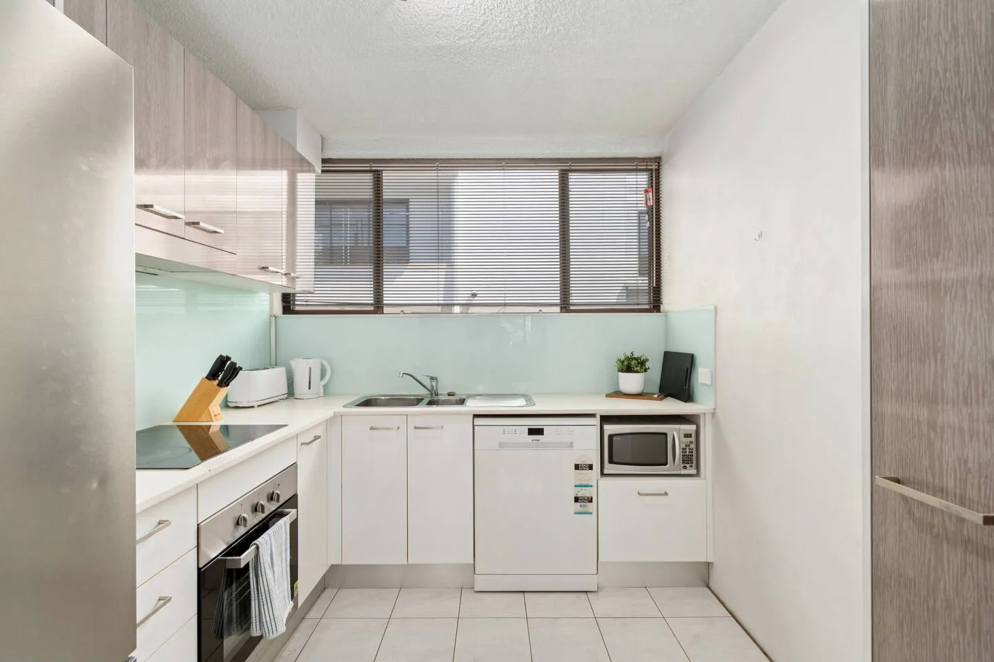 A compact kitchen has white cabinets, a tiled floor, and a window above the counter.