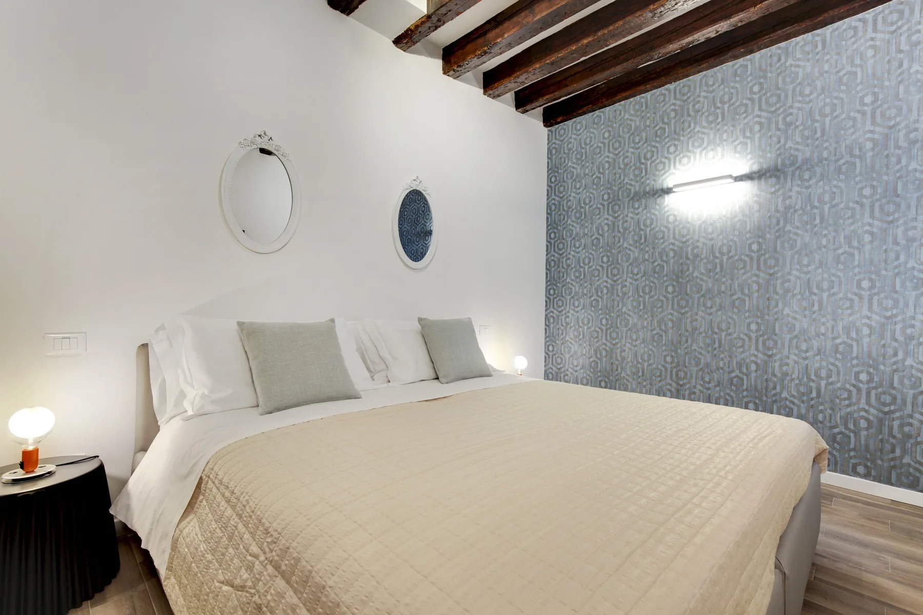 Un dormitorio con una cama grande, ropa de cama clara y papel pintado estampado.