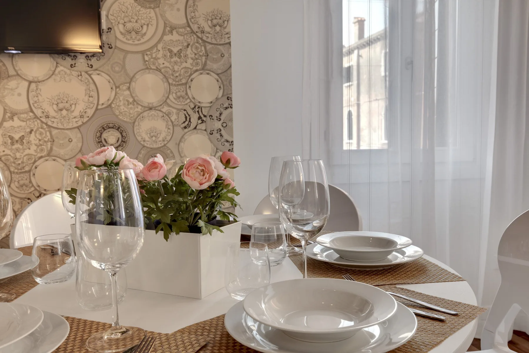 Una mesa de comedor está puesta con platos y copas junto a un jarrón con flores.