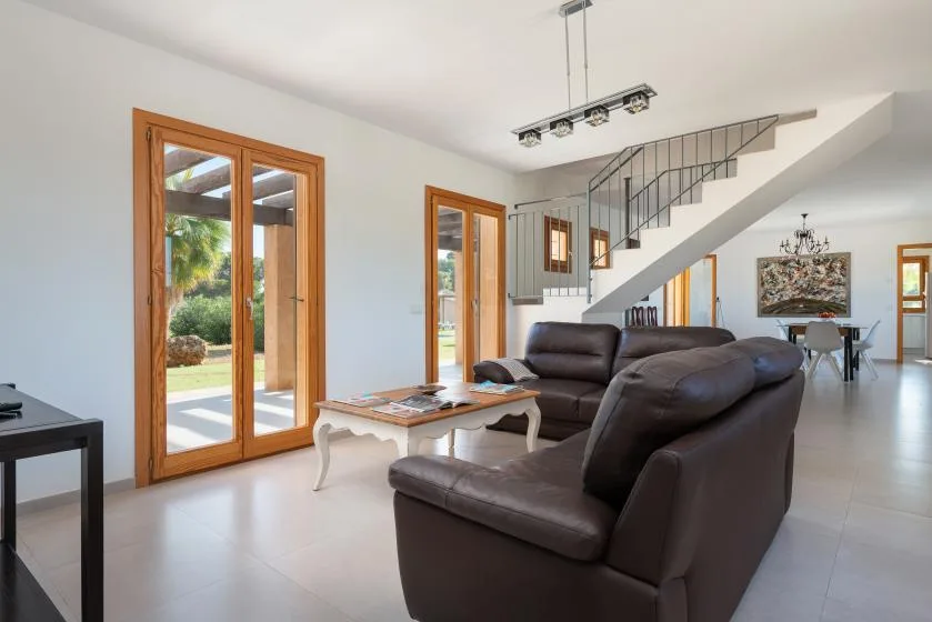 A bright living room with dark seating, a low table, and glass doors opening to a garden.