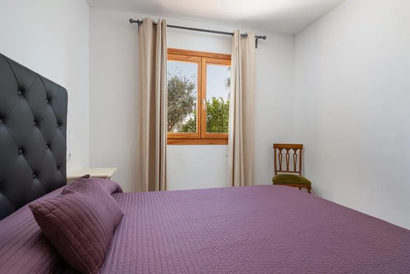 A bedroom with a purple bedspread, a curtained window, and a wooden chair.