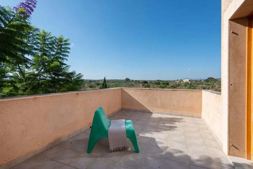 A sunlit terrace with a tiled floor and a low peach-colored wall overlooks greenery.