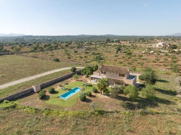 A countryside house and swimming pool sit amid open fields and scattered trees.