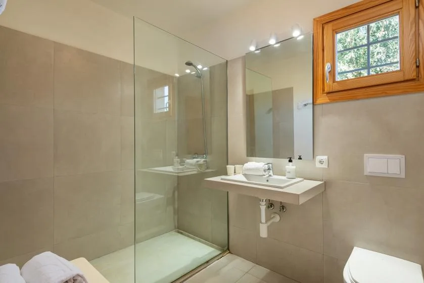 A tiled bathroom with a glass shower, sink, and window.