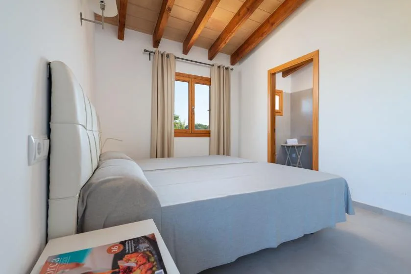 A bedroom with a bed beneath exposed wooden ceiling beams.