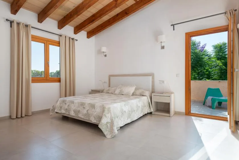 A bright bedroom with a bed and an open doorway to a leafy outdoor space.