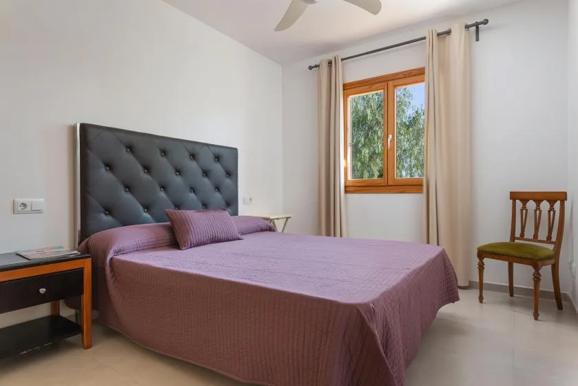 A bedroom with a bed, a window, and a wooden chair.