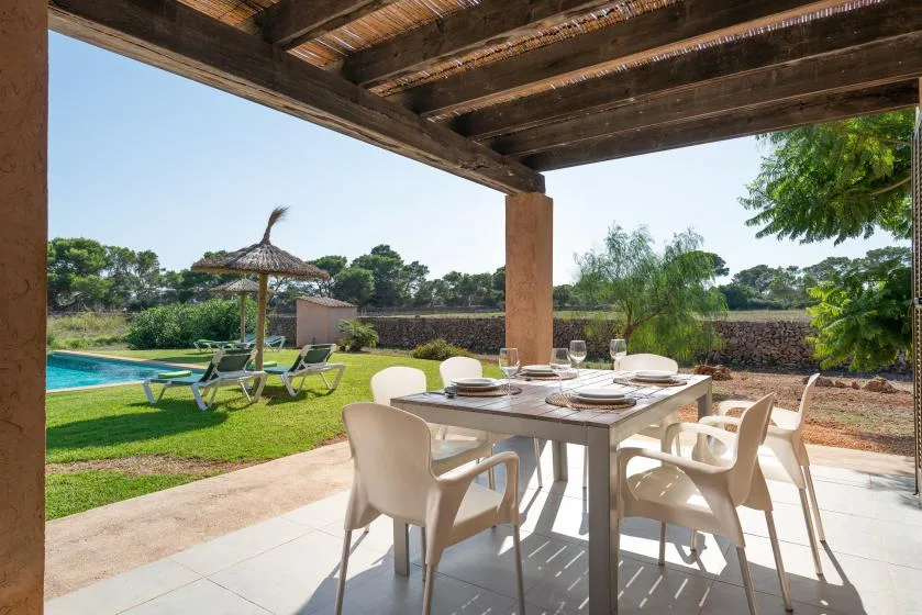 A covered outdoor dining area overlooks a garden, swimming pool, and thatched parasol.