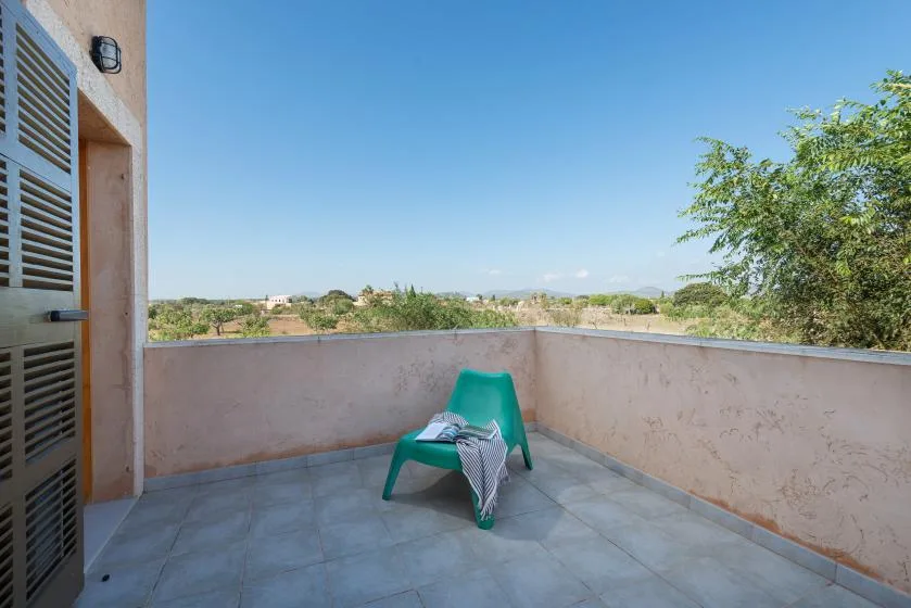 A tiled outdoor terrace has a green seat and views of trees and hills.
