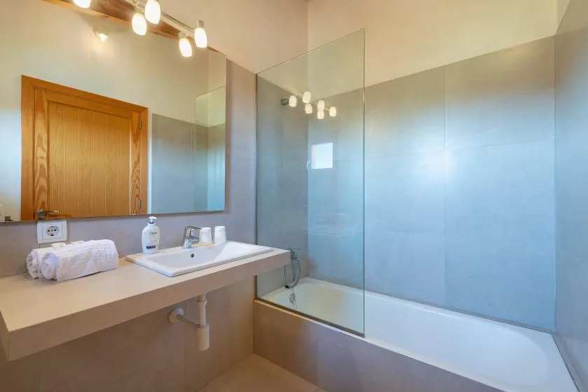 A bright bathroom with a sink, mirror, and glass shower screen.