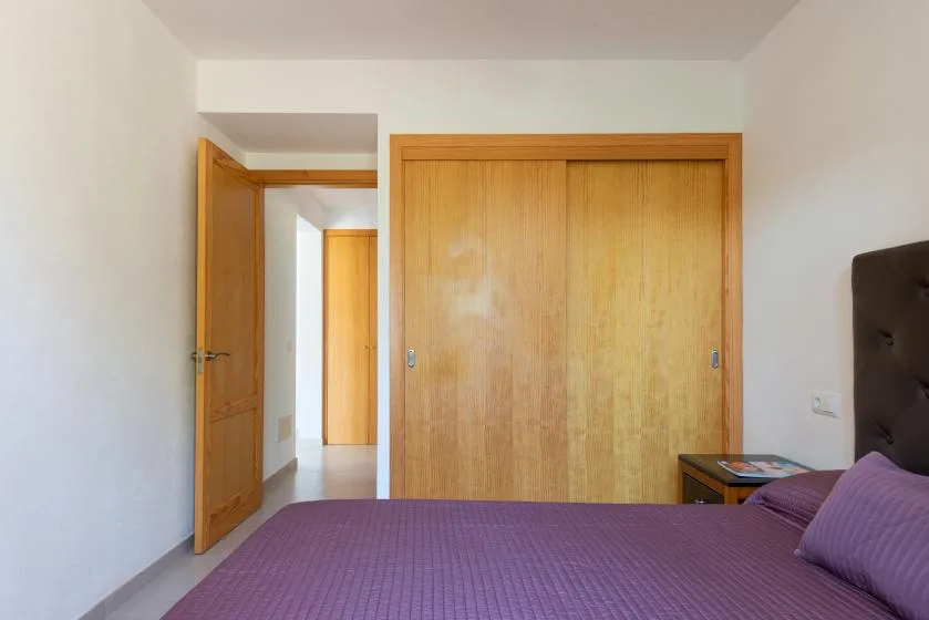 A bedroom with a purple bedspread, wooden closet doors, and an open doorway.