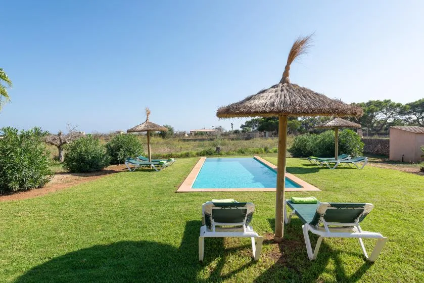 A garden pool area with sun loungers beneath thatched parasols.