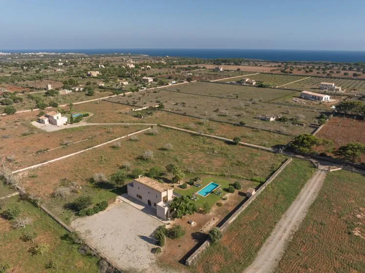 Aerial view of rural homes and fields, with the sea visible on the horizon.