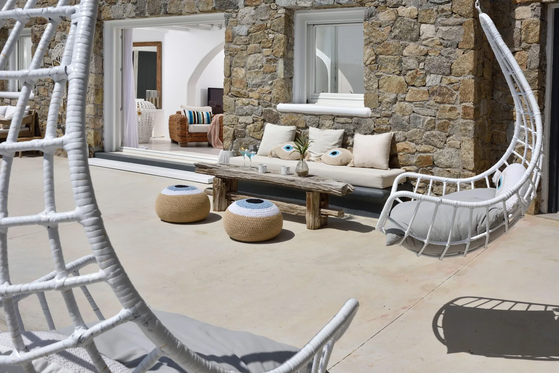 A stone-walled patio has a cushioned bench and woven poufs.