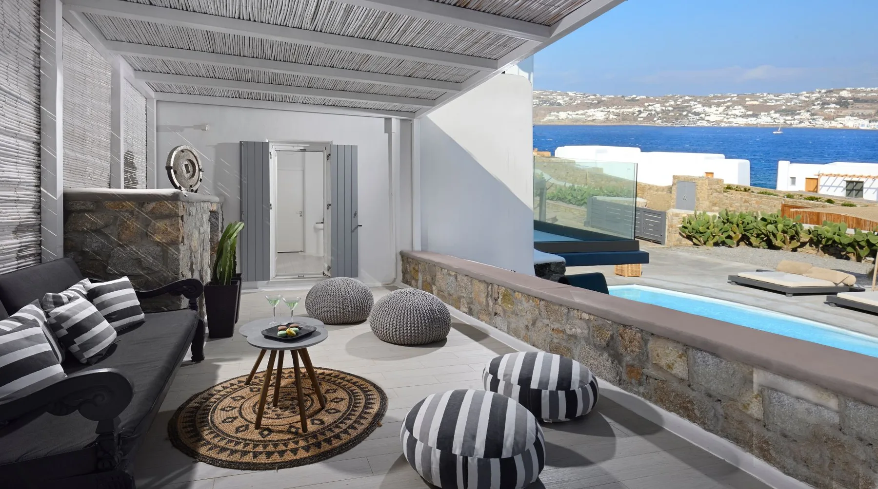 A shaded outdoor seating area overlooks a swimming pool and the sea.