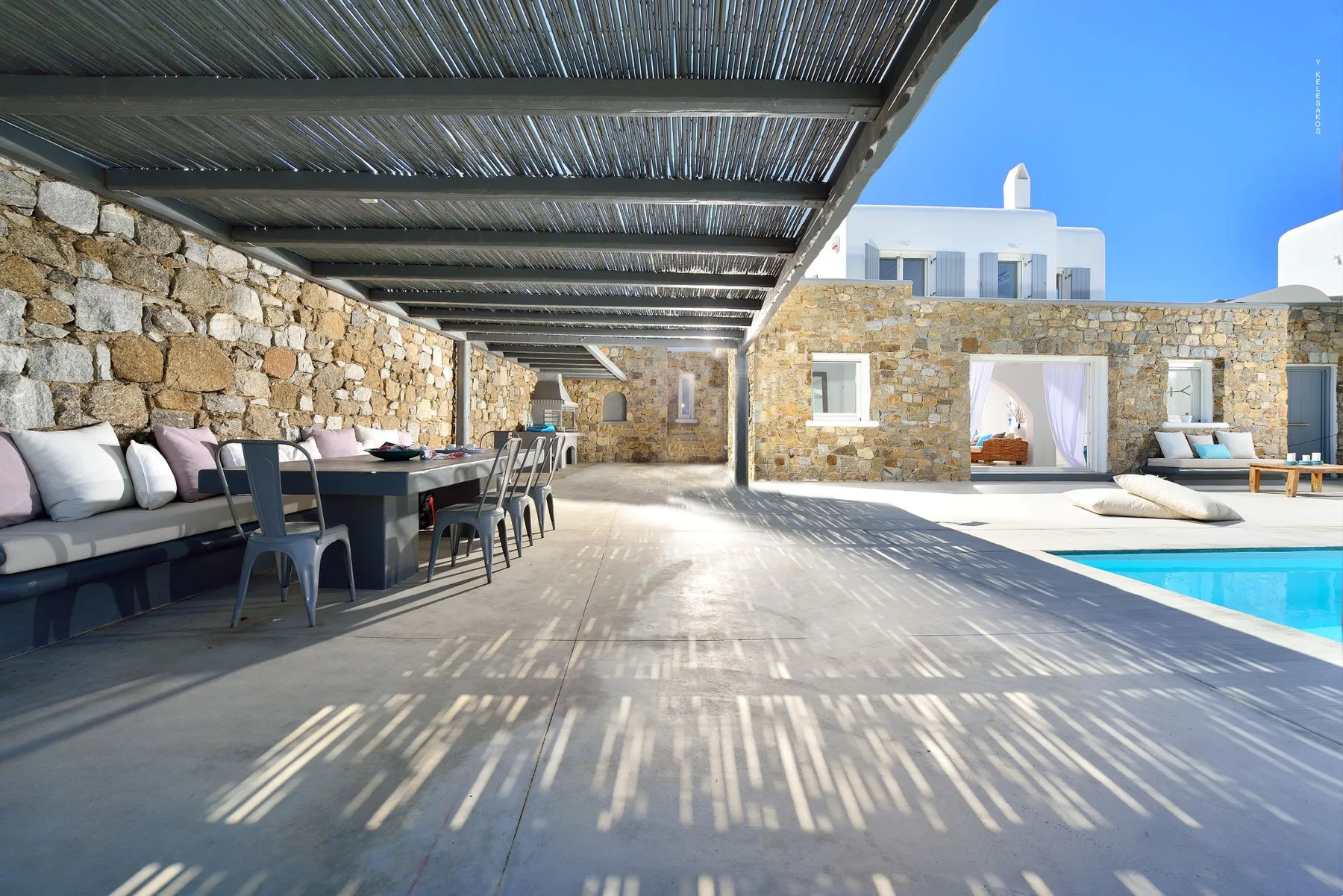 A covered outdoor dining area beside a stone building and swimming pool.
